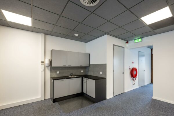 Kleine keukenhoek in een modern kantoor aan de De Ruijterkade met brandhaspel en nooduitgang.